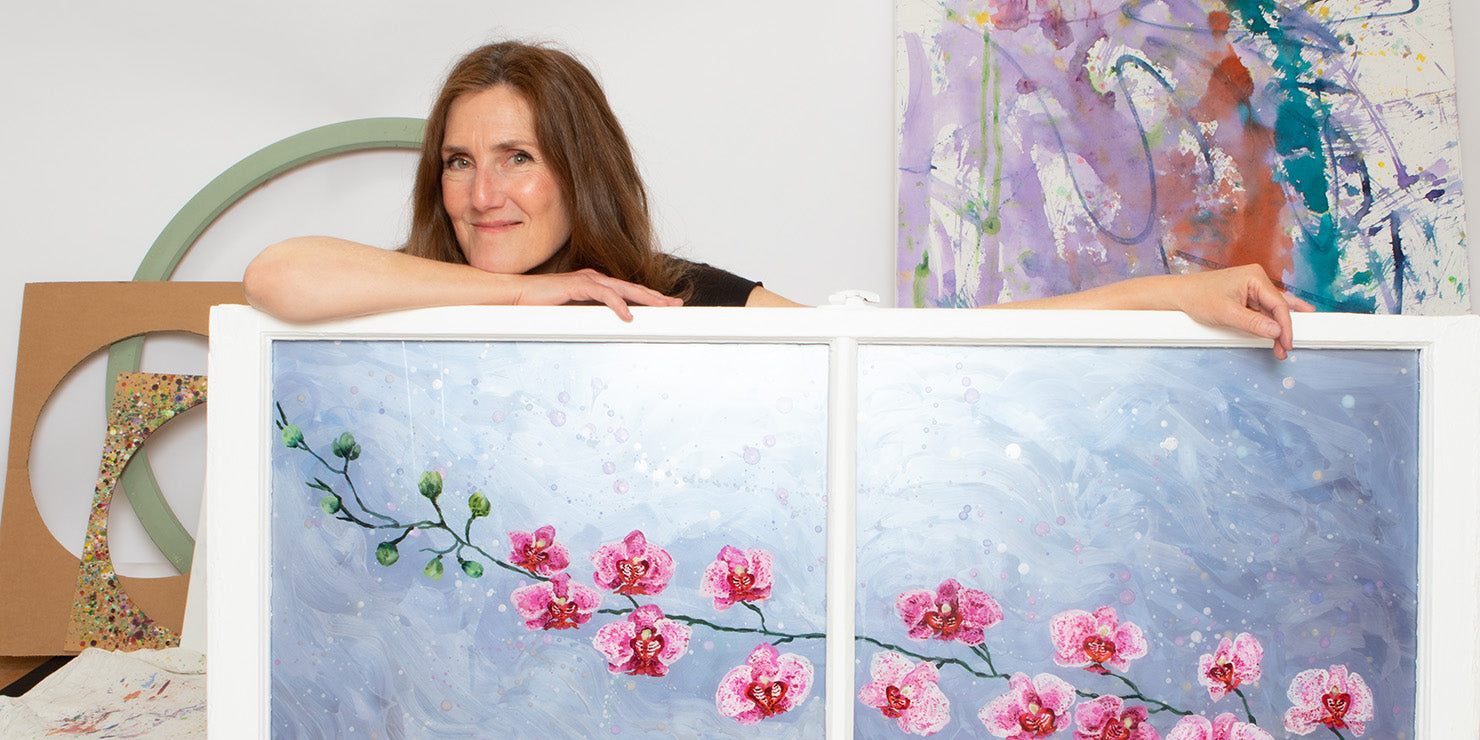 Rachel Shultz holding a recently completed painting in window (Speckle Orchids 2)
